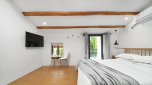 Une chambre à coucher comprenant un lit, un bureau, une chaise, un téléviseur fixé au mur et une fenêtre donnant sur un paysage verdoyant.