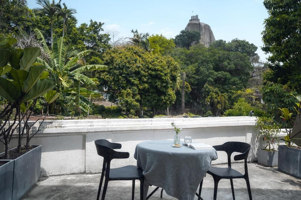 Una terraza con dos sillas negras y una mesa, rodeada de plantas en macetas y vistas a una gran estructura de piedra.