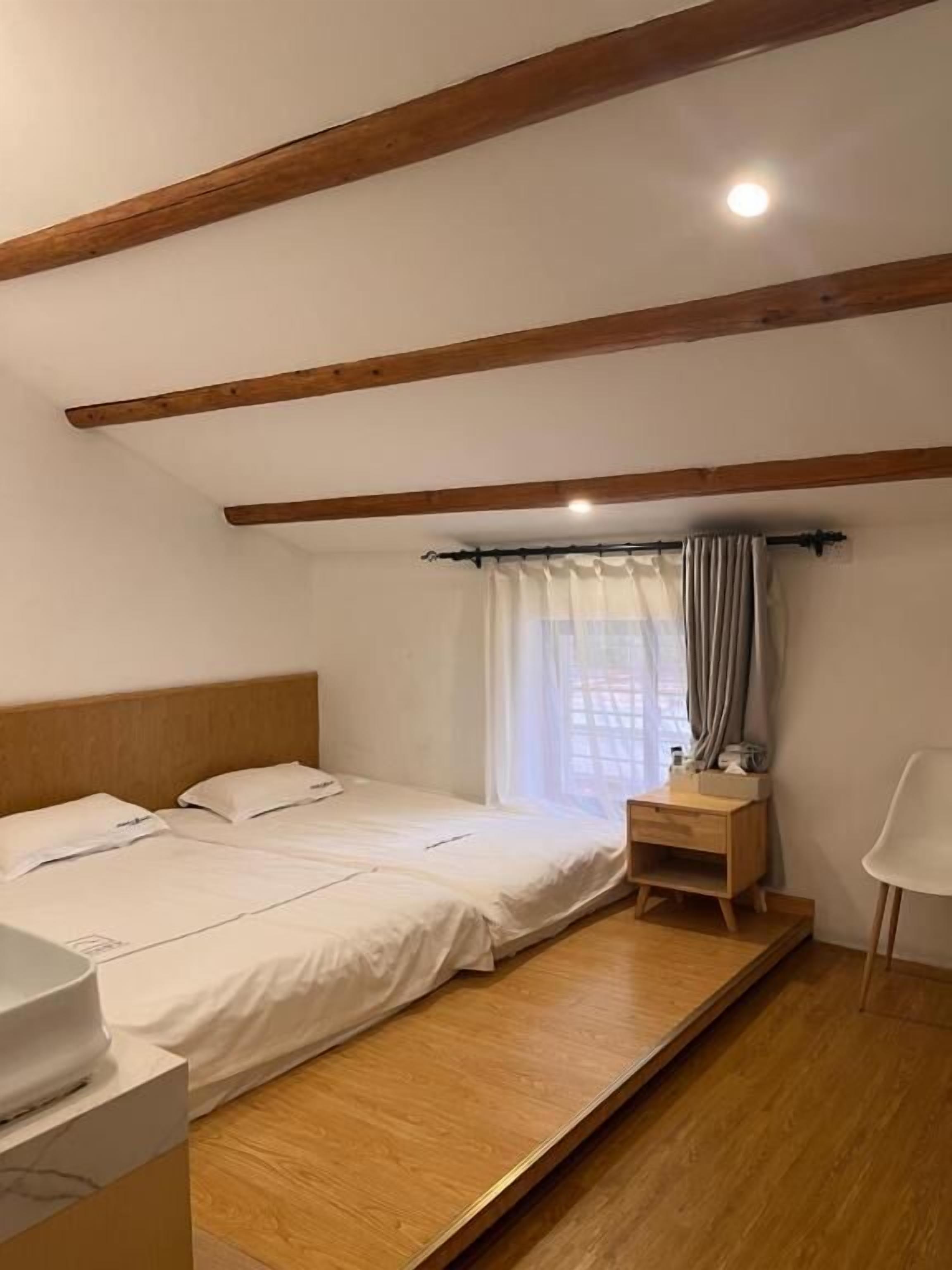 A bedroom with two beds, a wooden headboard, a bedside table, a chair, and a window with curtains.