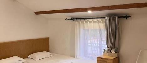 A bedroom with two beds, a wooden headboard, a bedside table, a chair, and a window with curtains.