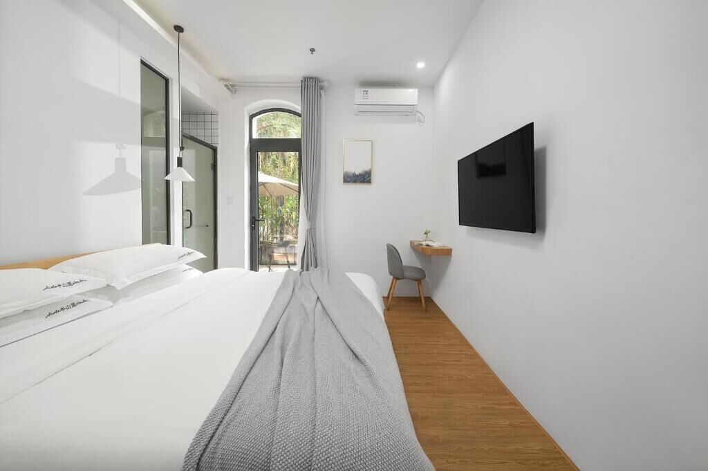 A modern hotel room with a bed, a desk, a chair, a TV, and a view of the outdoors.