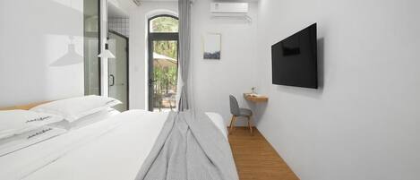 A modern hotel room with a bed, a desk, a chair, a TV, and a view of the outdoors.
