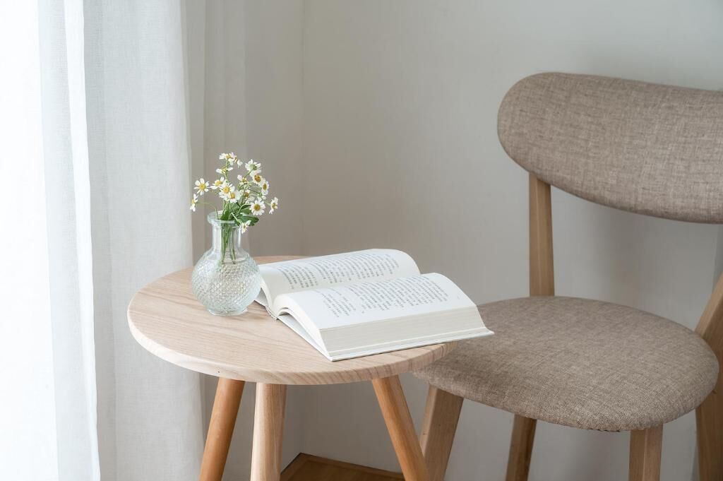 Et rundt træbord med en vase blomster og en åben bog.