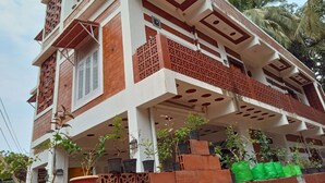 A multi-story building with a balcony, potted plants, and a decorative facade. - DhruvDhanush(2-bedroom with AC/2 attached bathroom in lovely Ullal/deralakatte (Ullal)