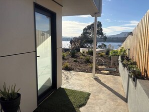 Uma casa moderna com porta de vidro, um pátio de concreto e vista para um lago.