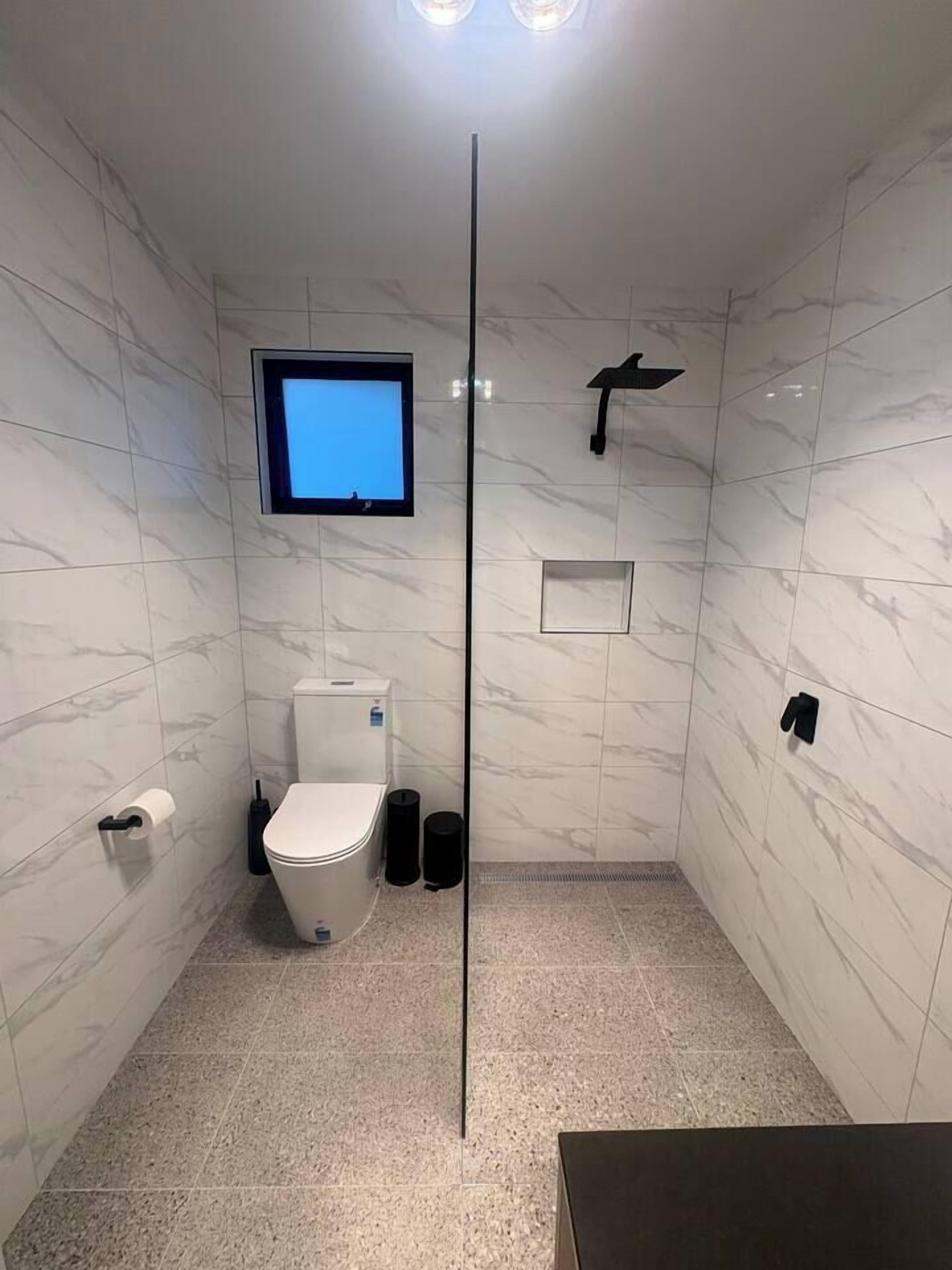Un baño moderno con inodoro, televisor montado y cabezal de ducha.