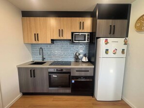 Eine kleine Küche mit Holzschränken, einer Mikrowelle, einem K ühlschrank und einem Spülbecken.