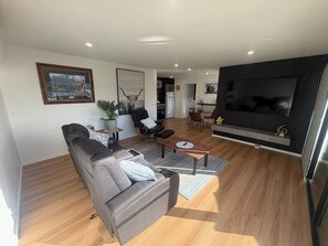 Ein modernes Wohnzimmer mit Sofa, Couchtisch und Fernseher. Es gibt einen Essbereich mit Stühlen und einem Tisch.