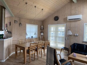 Ein Zimmer mit Holzwandverkleidung, einem Esstisch, Stühlen, einem schwarzen Sofa, einer Uhr und einer Klimaanlage.