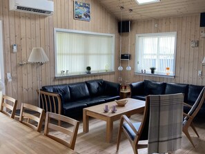 Ein Zimmer mit einer schwarzen Ledersofa, Holzstühlen, einem Holztisch und großen Fenstern mit Jalousien.