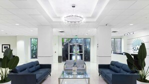 A modern lobby with two sofas, a glass coffee table, a chandelier, and a reception desk with a sign. - Oceanview Comfort Elegant S Ocean Drive (Hollywood)