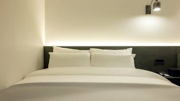 A neatly made bed with white linens, a dark headboard, and a wall-mounted light fixture.