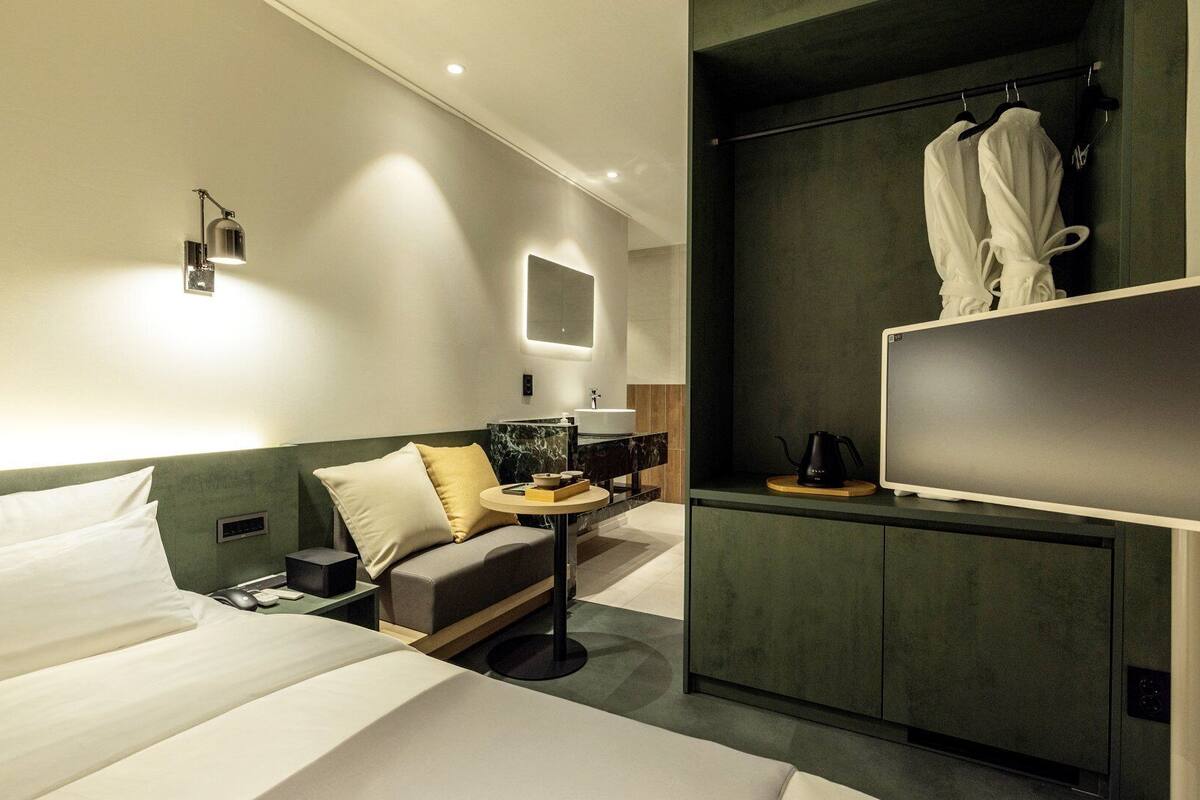 A modern hotel room with a bed, a desk, a chair, a TV, and a wardrobe.