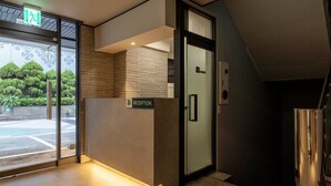 Zona de recepción con puerta de vidrio, mostrador de recepción y un cartel que dice 'Reception'.