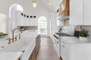 A modern kitchen with white cabinetry, a large island with a sink, and a gas range. - Terra Luxe @ Lake Conroe; Luxury Golf and Lake Retreat at April Sound (Conroe)