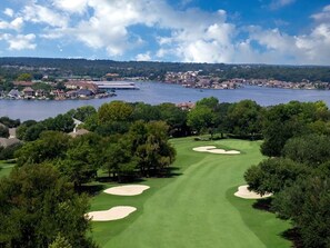 A golf course with sand bunkers, a water body, and residential buildings in the background. - Terra Luxe @ Lake Conroe; Luxury Golf and Lake Retreat at April Sound (Conroe)