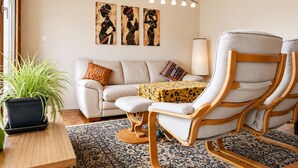 Ein Wohnzimmer mit einer Couch, zwei Sesseln, einem Couchtisch, einer Lampe und Kunstwerken an der Wand.