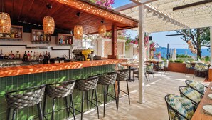 An outdoor bar area with a wooden ceiling, wicker chairs, and a view of the sea.