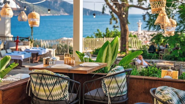 An outdoor dining area with tables and chairs, a view of the sea, and hanging lanterns.