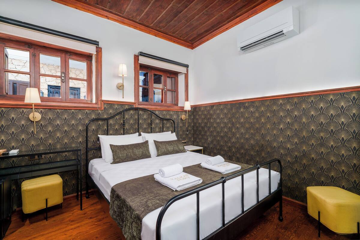 Quarto com uma cama, duas mesas de cabeceira, escrivaninha, cadeira e ar condicionado.