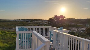 Une terrasse avec des chaises et une balustrade donnant sur un paysage naturel au coucher du soleil.