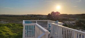 Eine Terrasse mit Stühlen und Geländer mit Blick auf eine natürliche Landschaft bei Sonnenuntergang.