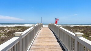 Une promenade en bois menant à une plage où flotte un drapeau américain.