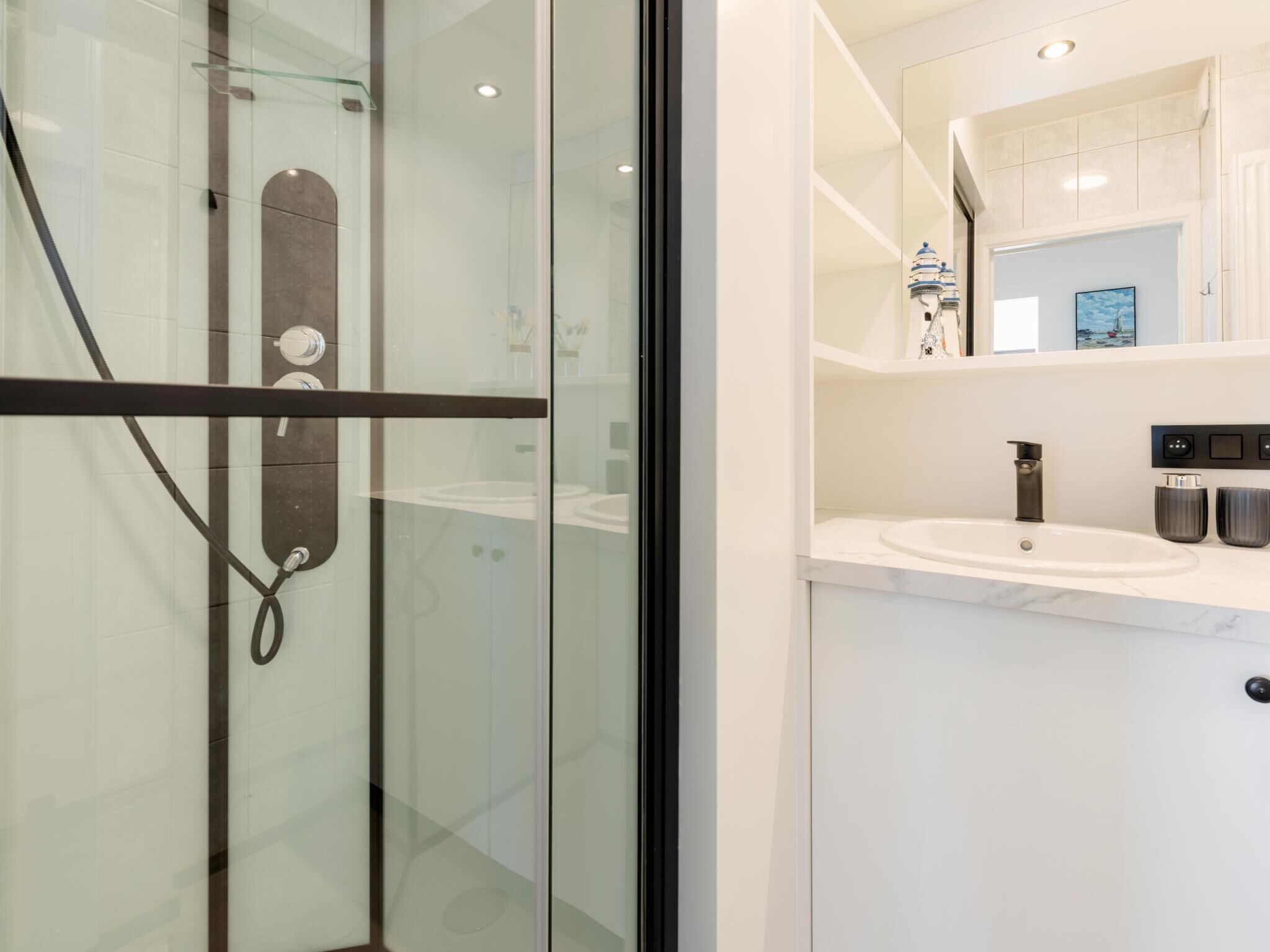 Ein modernes Badezimmer mit Duschkabine aus Glas, einem weißen Waschbecken und einem Spiegel darüber.