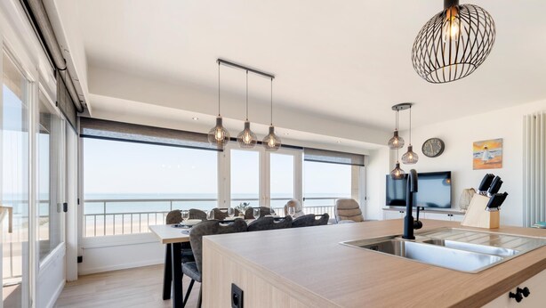 A modern kitchen with a large island, pendant lights, and a view of the sea. - Sea view and comfort in Middelkerke (Middelkerke)