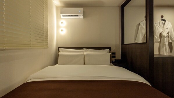 Habitación de hotel con una cama, un equipo de aire acondicionado y un espejo con una bata.