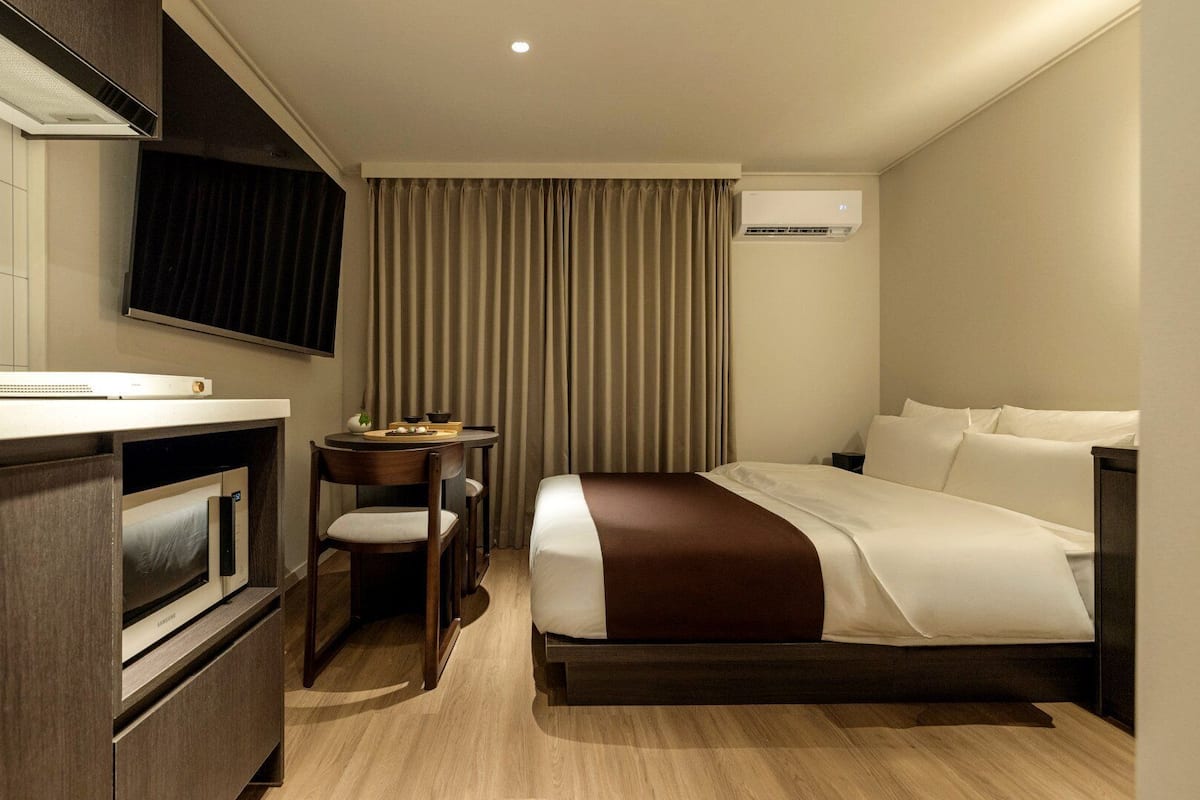 Habitación de hotel con cama, escritorio, silla, televisor de pantalla plana y aire acondicionado.