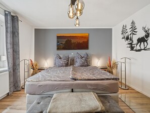 A bedroom with a large bed, bedside tables, a hanging light fixture, a painting, and a wall decal. - Apartment in Straßberg in the Harz Mountains (Straßberg)