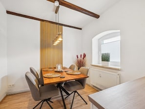 Ein Essbereich mit einem Holztisch, vier Stühlen, einer Hängelampe, einem Fenster mit Jalousien und einer Heizung.