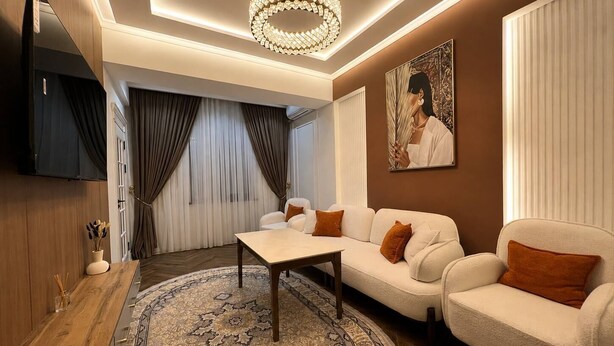 A modern living room with a sofa set, a coffee table, a TV mounted on the wall, and a decorative chandelier.