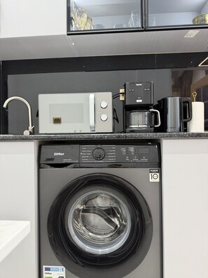 Eine kleine Küche mit Waschmaschine, Mikrowelle und Kaffeemaschine.