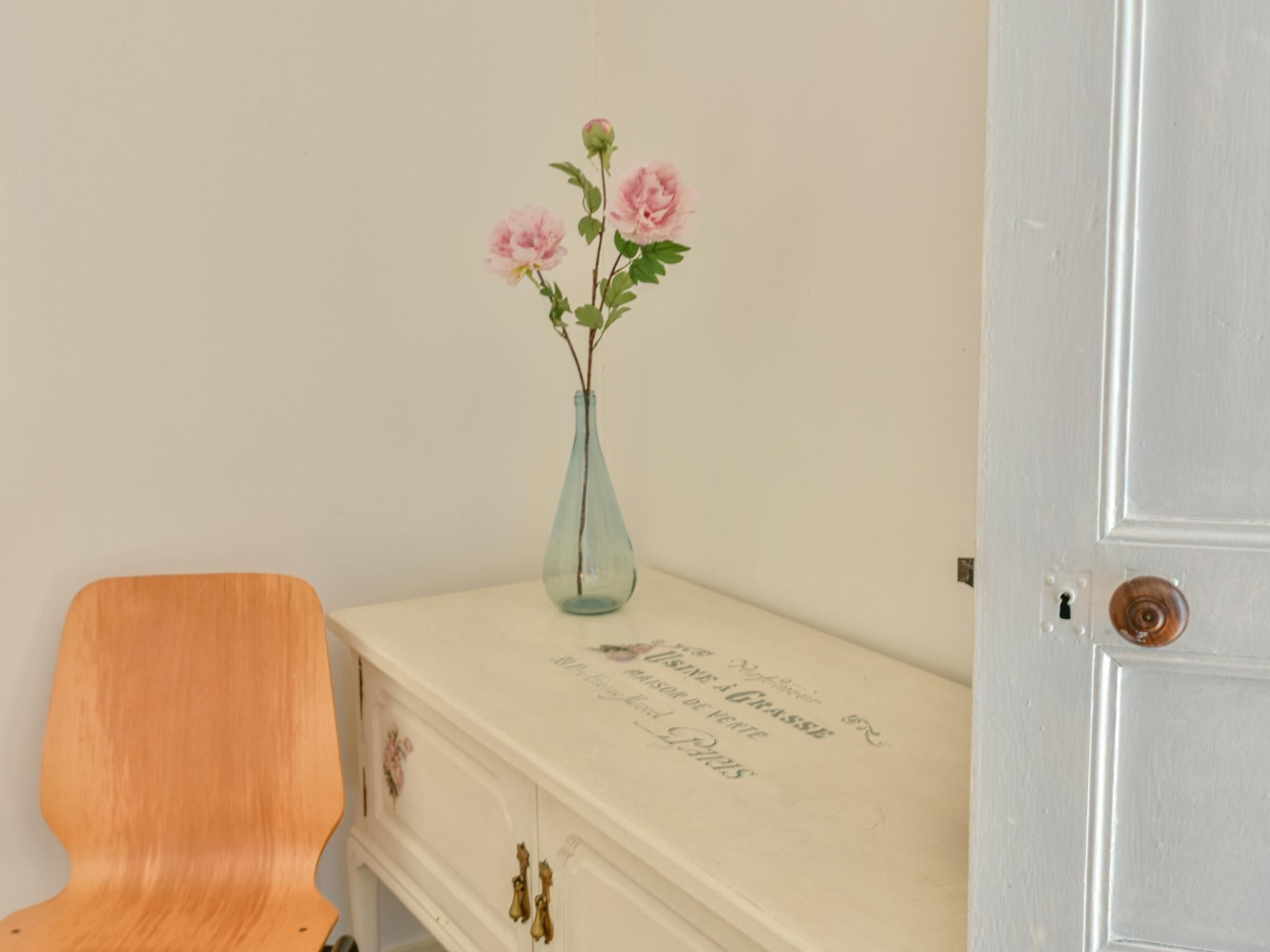A wooden chair next to a white dresser with a vase of flowers and a door with a round handle.