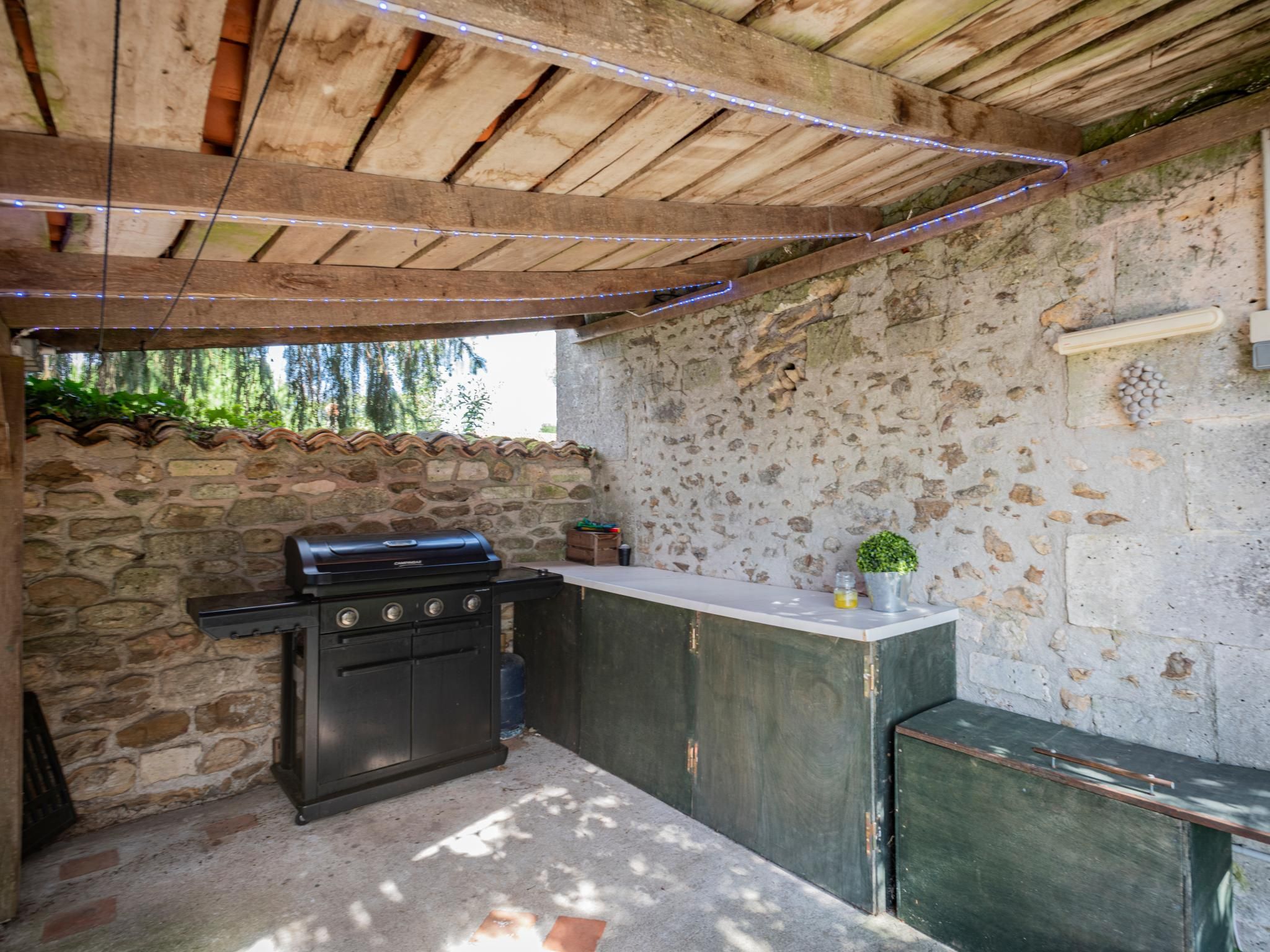 An outdoor kitchen area with a grill, a stone wall, and a wooden ceiling.