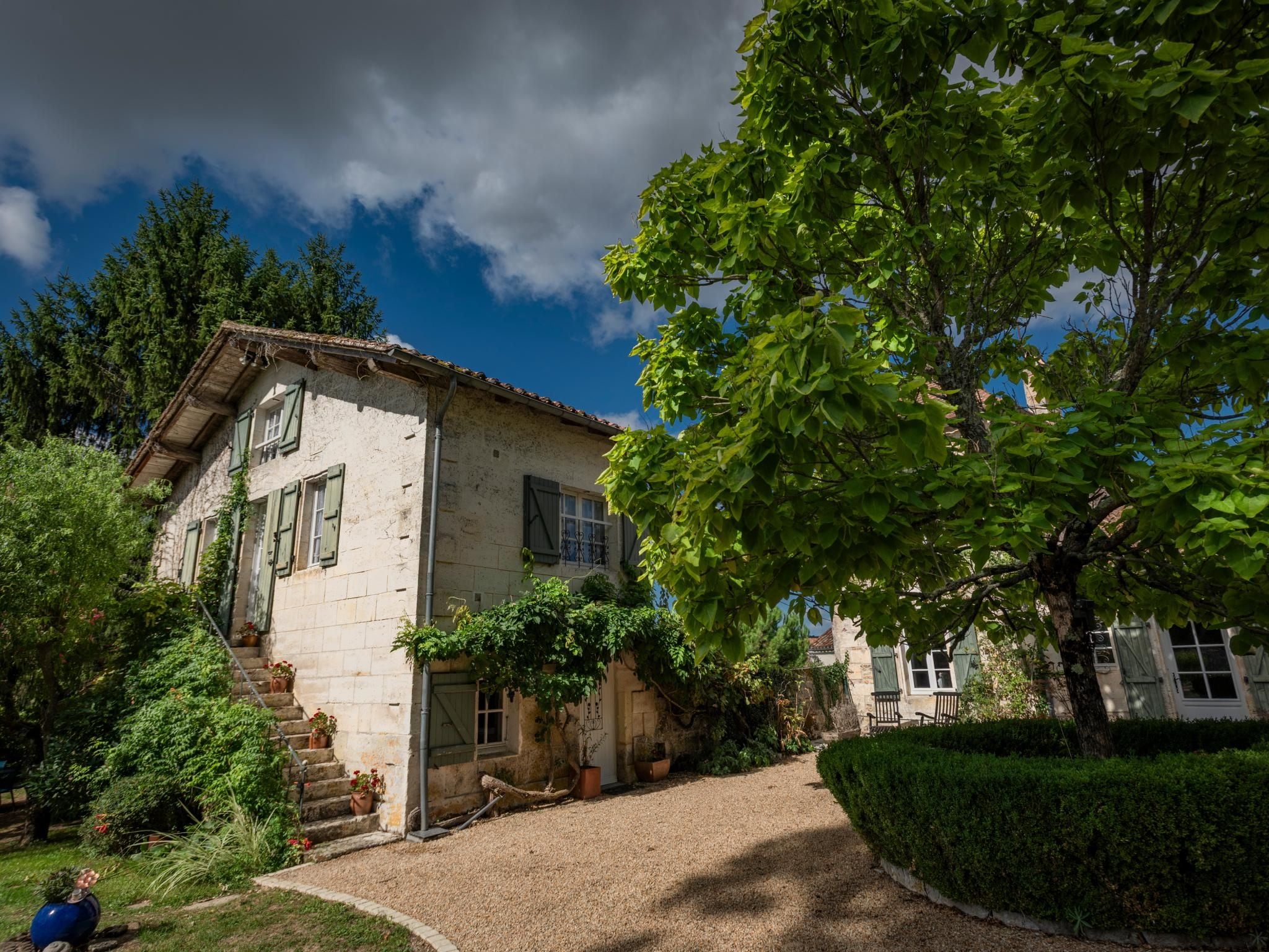 A stone house with a traditional design, featuring a staircase leading to the entrance, surrounded by lush greenery and a clear sky.