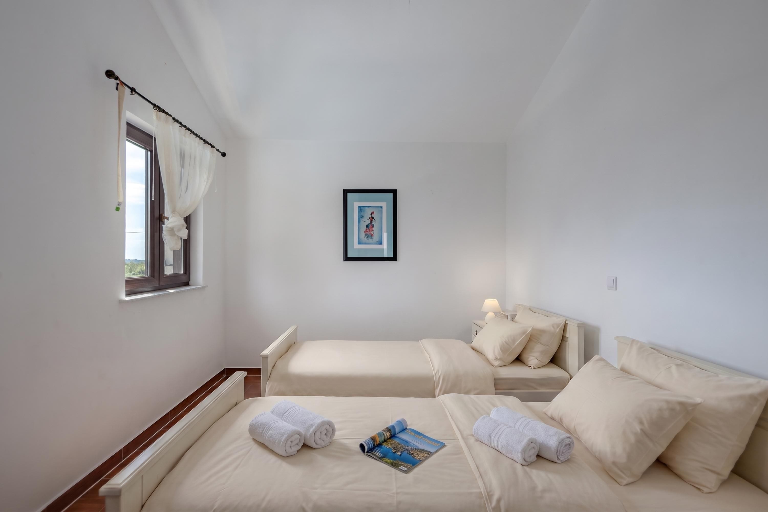 A hotel room with two beds, a window with curtains, a framed picture on the wall, and a magazine on the bed.