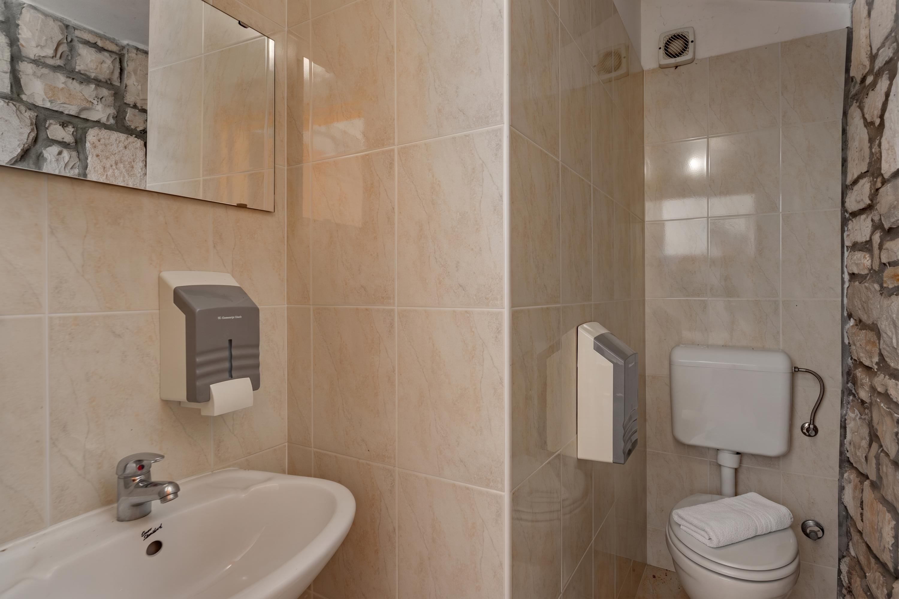 A bathroom with a sink, mirror, hand dryer, toilet, and a shower area.