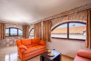 A room with stone walls, a sofa, a table with snacks and a glass of wine, and large windows with curtains. - Pool House Suzi in Heart of Istria (Barban)