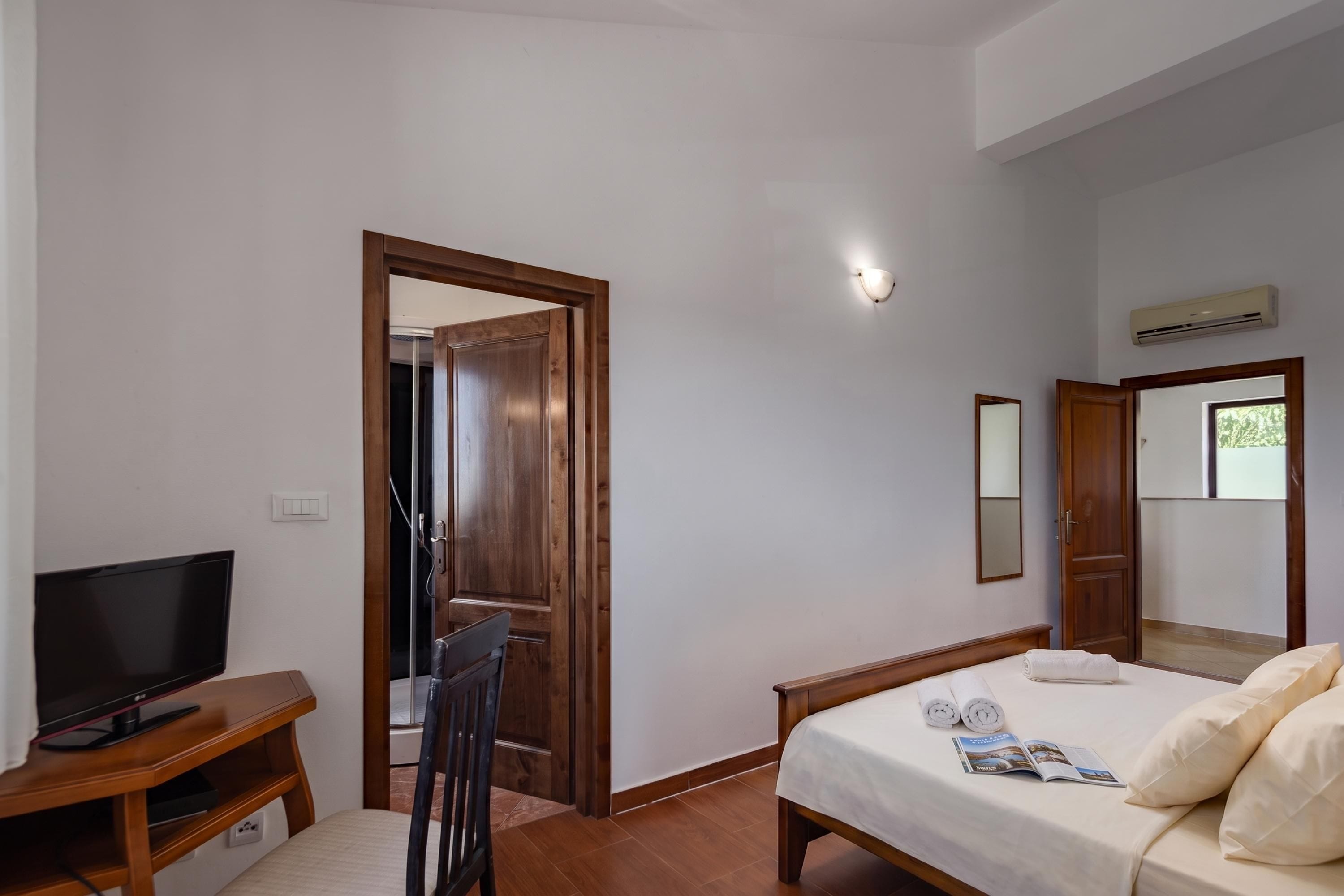 A hotel room with a bed, a TV, a desk, and a bathroom door.
