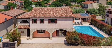 A villa with a swimming pool, stone arches, and a red-tiled roof.