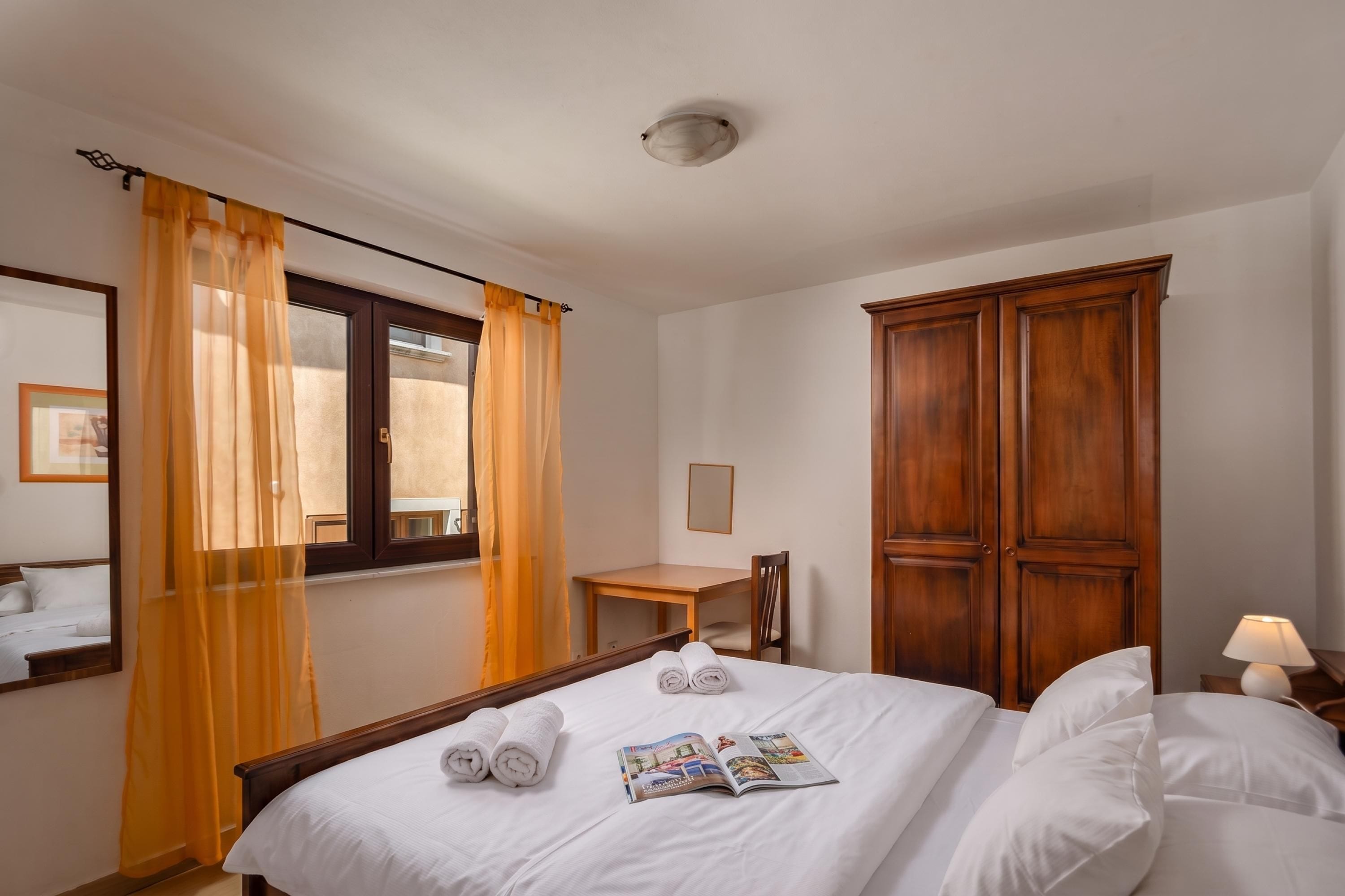 A hotel room with a bed, a wooden wardrobe, a desk, and a chair.