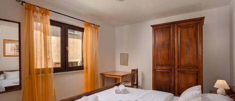 A hotel room with a bed, a wooden wardrobe, a desk, and a chair.