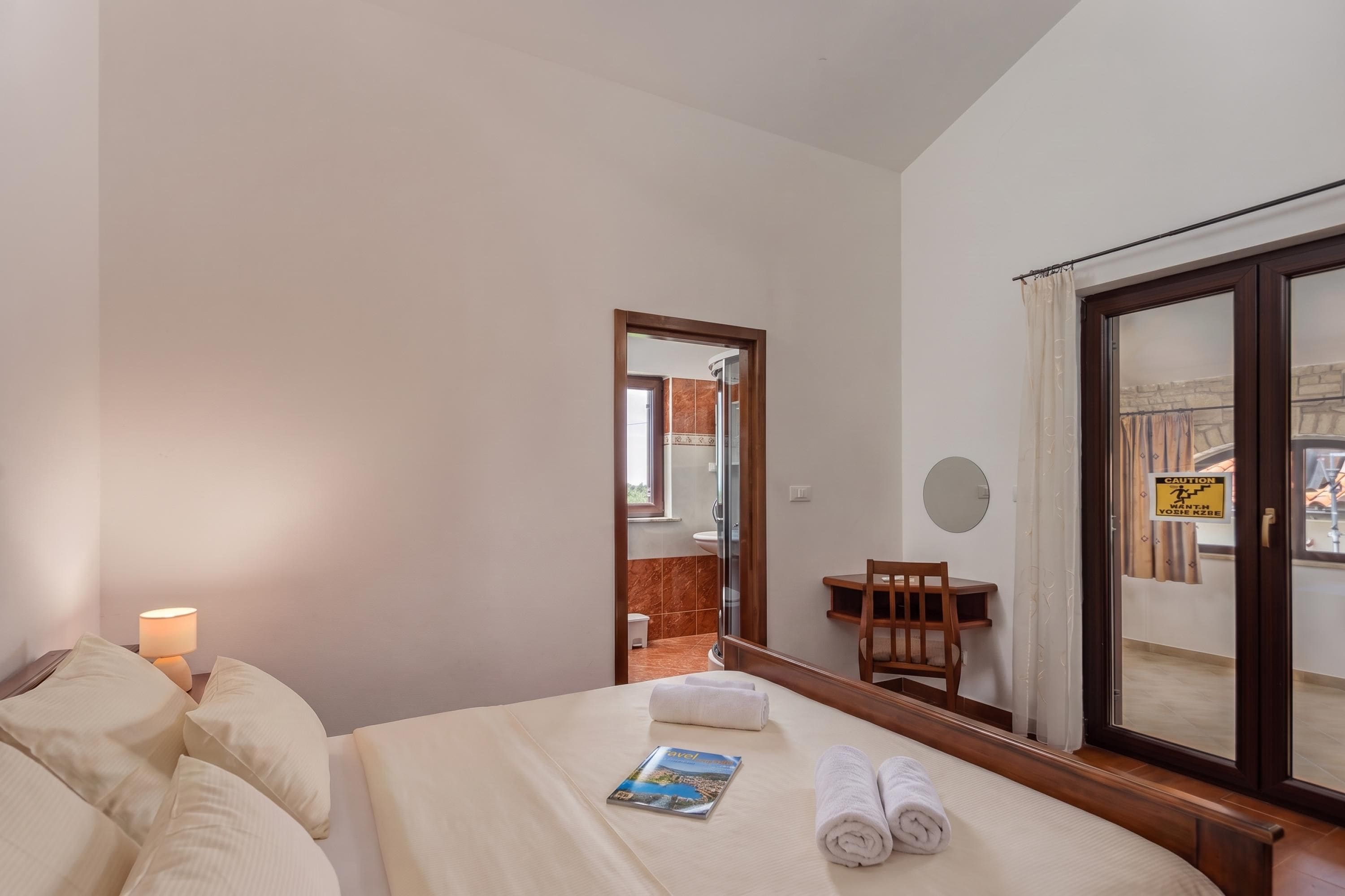 Una habitación de hotel con una cama, una mesita de noche con lámpara, una pequeña mesa con una silla y una ventana con vistas al exterior.