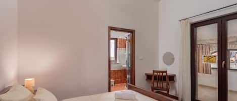 Una habitación de hotel con una cama, una mesita de noche con lámpara, una pequeña mesa con una silla y una ventana con vistas al exterior.