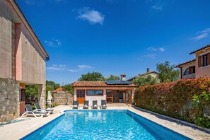 A swimming pool with lounge chairs, a stone wall, and a small building with a tiled roof. - Pool House Suzi in Heart of Istria (Barban)