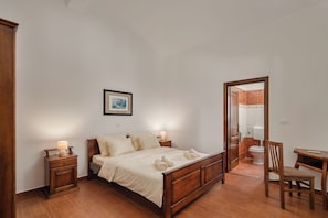 A bedroom with a wooden bed, nightstands, a chair, a desk, and a bathroom visible through an open door. - Pool House Suzi in Heart of Istria (Barban)