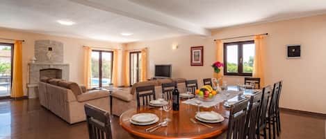 A spacious living area with a fireplace, a sofa, a dining table set for six, and a television.